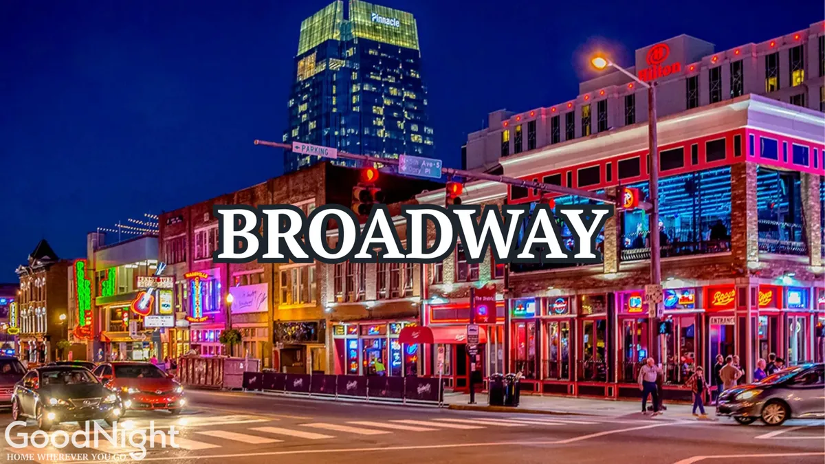 This captivating exterior image captures the buzz of downtown Nashville with neon signs illuminating crowded streets lined with colorful storefronts and tall buildings. People are seen dining, shopping, and enjoying live music along the iconic Broadway strip.
