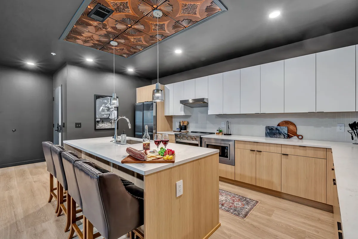 A welcoming kitchen area featuring a kitchen island with bar stools, a stylish chandelier, and a decorative ceiling. The space is warm and inviting, perfect for both quick breakfasts and social gatherings, and suggests the inclusion of starter kitchen amenities.