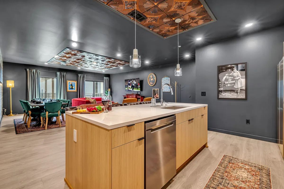 This image showcases a vibrant open kitchen and dining area connected by a decorative ceiling and enriched with wall art. The focus is on the kitchen island, dining space, and the seamless blend between cooking and entertaining zones, which are lit to emphasize sociability and warmth.