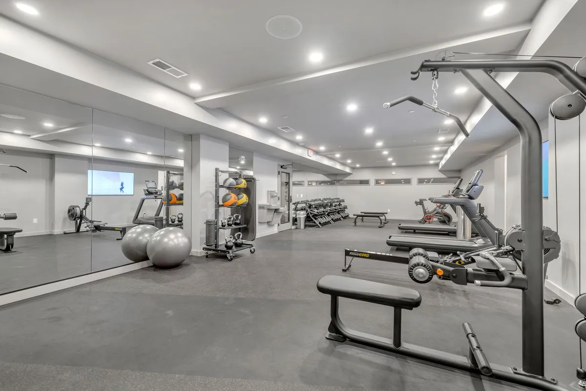 A bright, modern gym interior featuring a variety of exercise equipment such as fitness balls, strength machines, and mirrors. The layout encourages both personal workouts and group fitness activities.