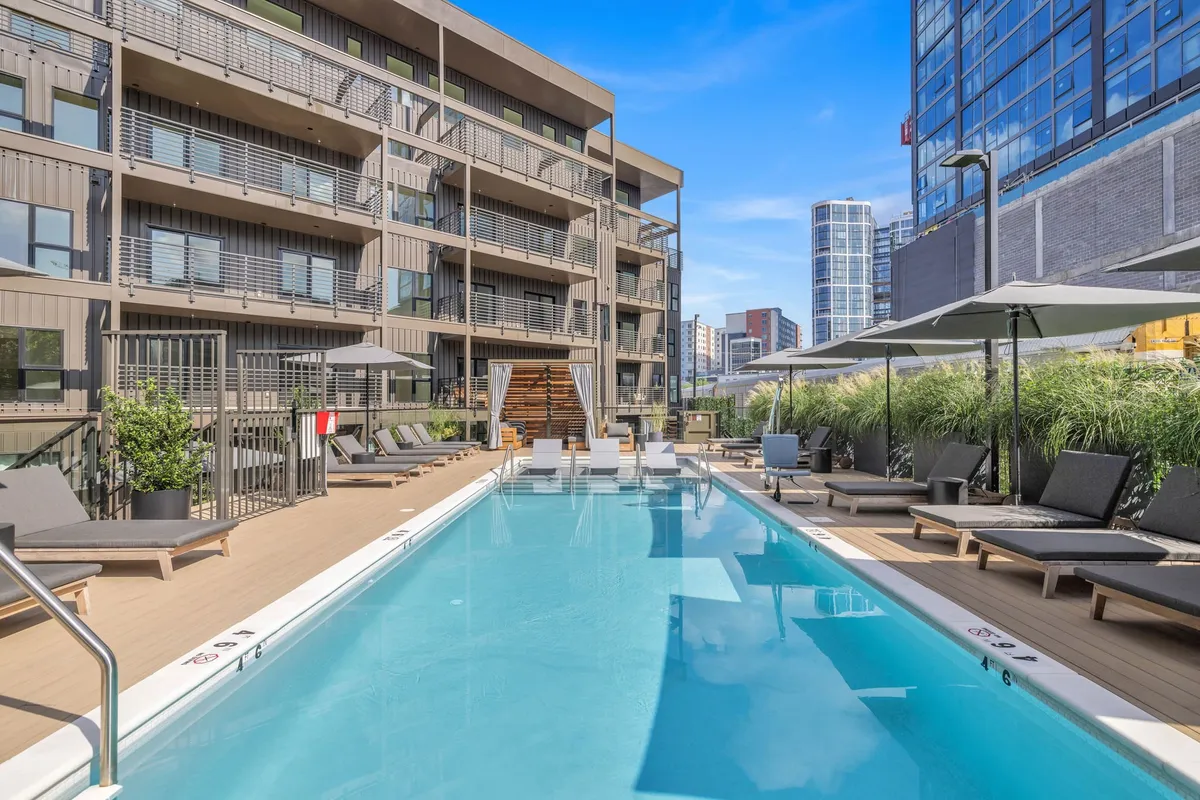 An inviting outdoor pool surrounded by lounge chairs and modern buildings, offering a relaxing yet social setting for guests. The pool area is perfect for group gatherings, whether for afternoon sunbathing or evening get-togethers under the sunset sky.