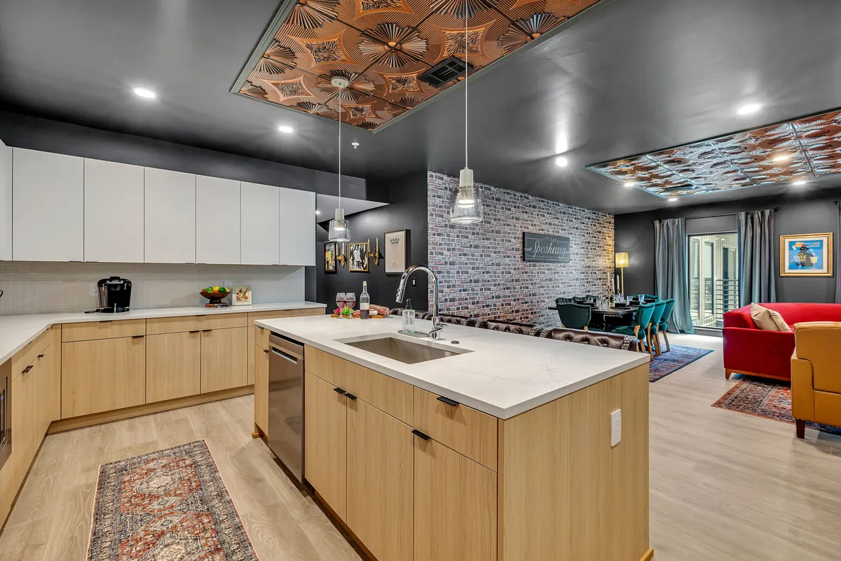 This image presents a kitchen and dining area with a striking kitchen island, exposed brick accents, and a decorative ceiling. The room is inviting and set up for both cooking and entertaining, with enough space for groups to gather comfortably.