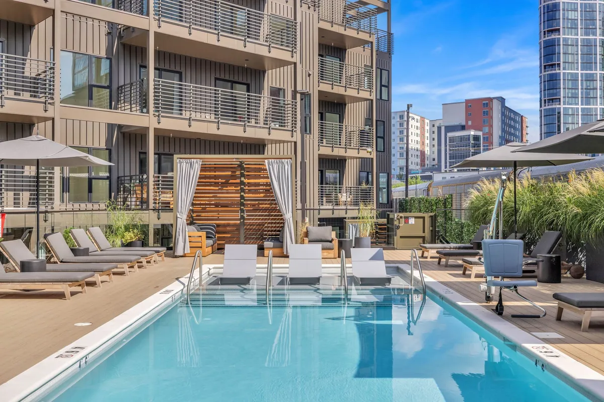 A vibrant, inviting pool area with lounge chairs, umbrellas, and the building’s facade in the background. The scene is set for family relaxation, swimming, and socializing during downtime at the property.