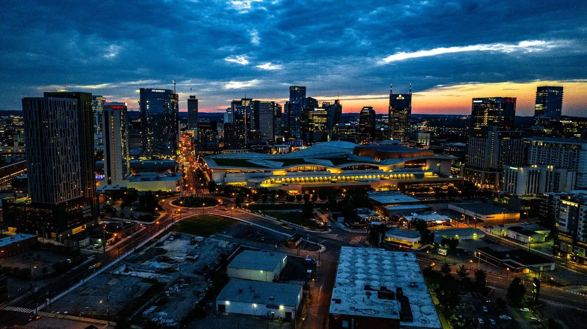 A breathtaking view of the Nashville city skyline at dusk, with illuminated buildings and street lights creating a lively urban atmosphere. The sky glows with the last light of day, and the city pulses with energy, hinting at vibrant nightlife and social adventures awaiting groups exploring downtown.